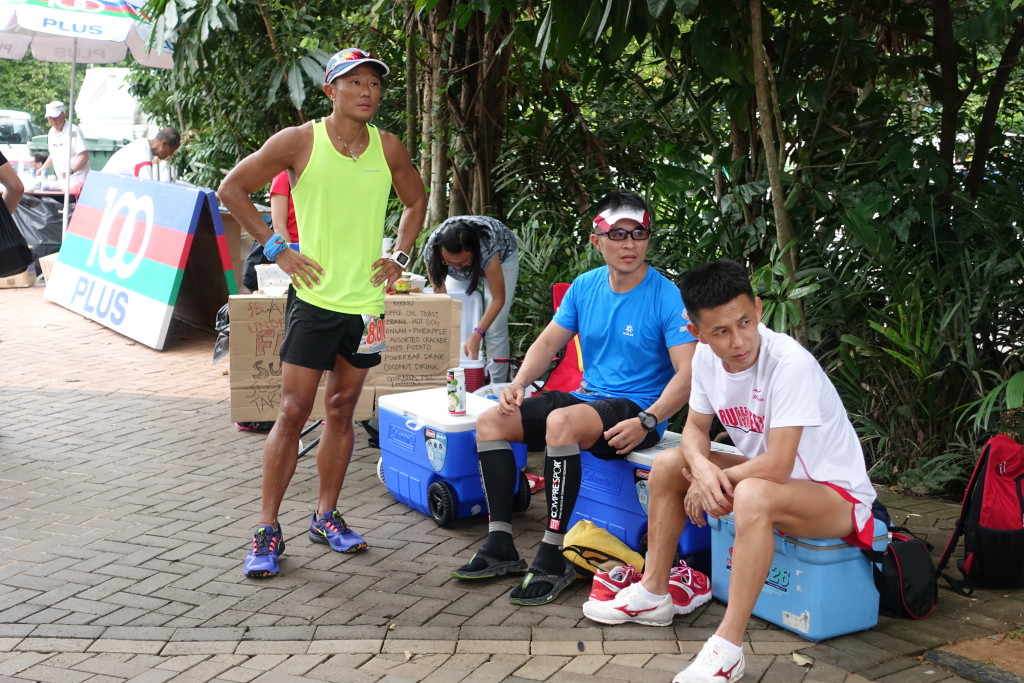 A runner takes a breather with two supporters looking on.